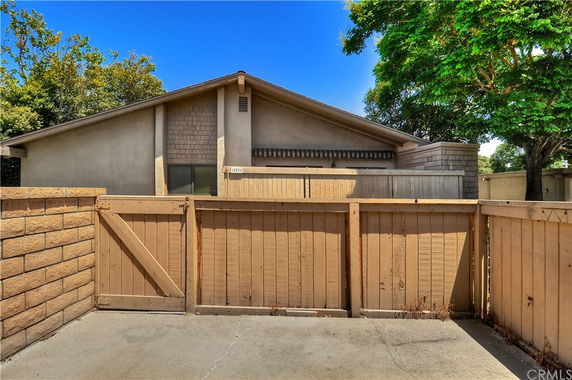 Front view of a single-story house with a wooden fence and paved pathway.