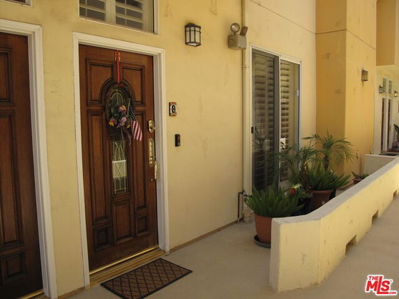 Front view of an entrance to a house with a wooden door and potted plants.