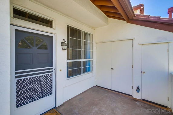 Entrance area of a house with a screen door, window, and two white doors on a porch.