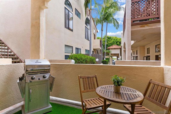 Outdoor patio area with a grill and wooden seating, view of nearby buildings.