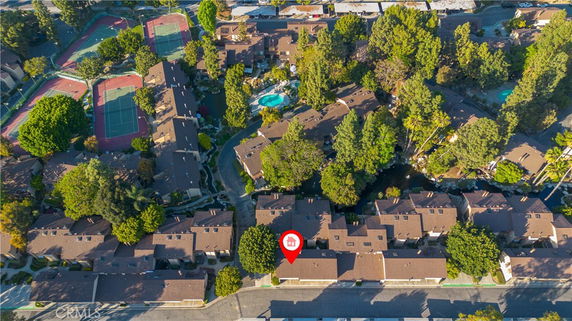 Aerial view of residential area with tennis courts and surrounding greenery.