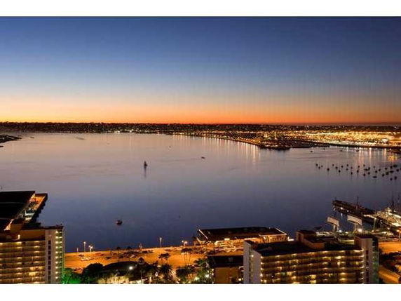 Wide angle view of a waterside cityscape at dusk with buildings and harbor lights.