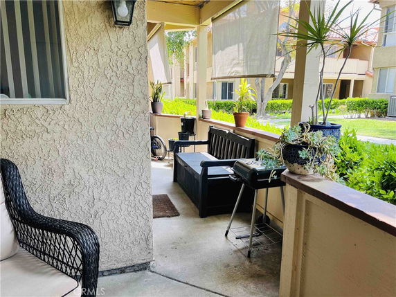 Outdoor view from a porch area with seating and plants, overlooking nearby buildings.