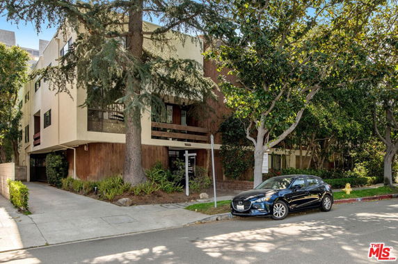 Front view of a multi-story building with trees and a parked car.