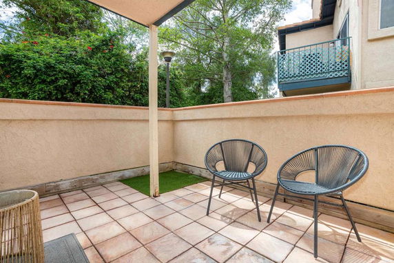 Outdoor patio area with two chairs and tiled flooring, surrounded by a low wall and greenery.