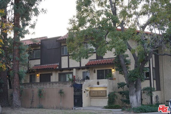 Front view of a two-story residential building with a gated entrance and overhanging trees.