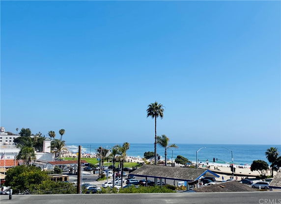 Panoramic view of a beach and ocean with buildings and palm trees in the foreground.