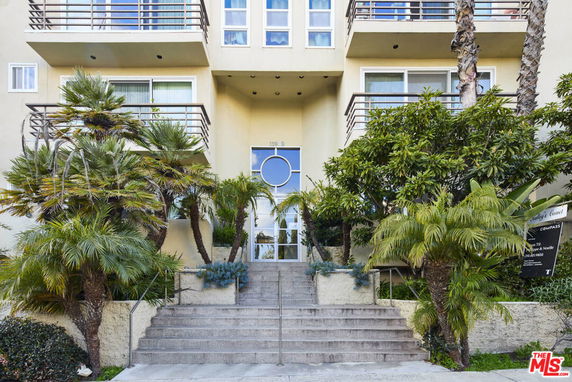 Front view of a multi-story building with balconies and a staircase leading to the entrance.