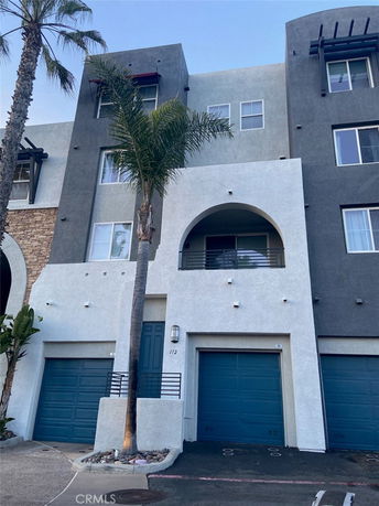 Front view of a multi-story residential building with arched balcony and garage doors.