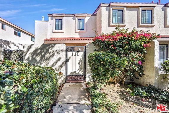Front view of a two-story house with a gate and bougainvillea.