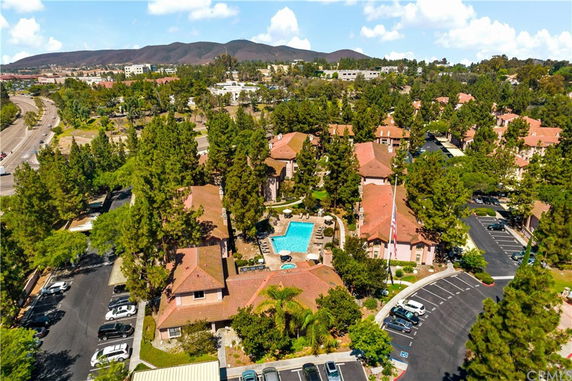 Aerial view of a residential community with multiple buildings, a central swimming pool, and surrounding green trees.