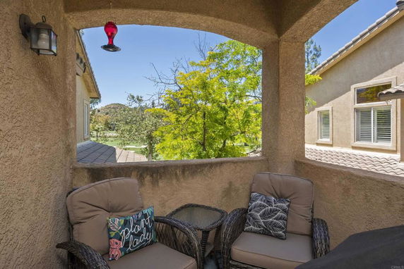 Balcony view from a house showing surrounding trees and neighboring building roof.