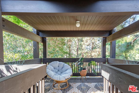 View from a patio or deck with a chair and plants, surrounded by trees.