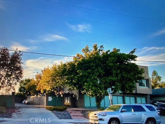 Front view of a two-story building with trees and parked cars.