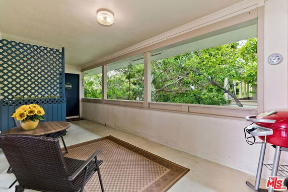 Covered outdoor area with seating and a grill, overlooking greenery.
