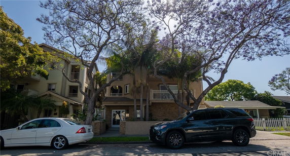 Front view of a multi-story building with balconies and surrounded by trees.