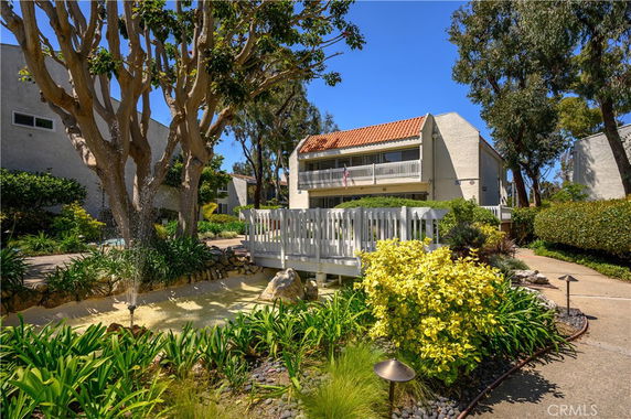 Front view of a two-story house with a balcony and a tiled roof, surrounded by landscaped garden.