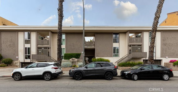 Front view of a multi-story building with balconies and cars parked in front.