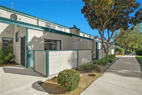 Front view of a multi-story residential building with green trim and a small fenced patio area.