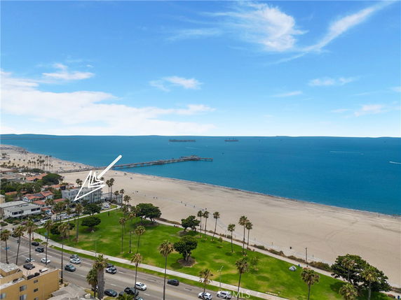 Wide-angle view of a coastline with a beach, pier, and buildings near the ocean.