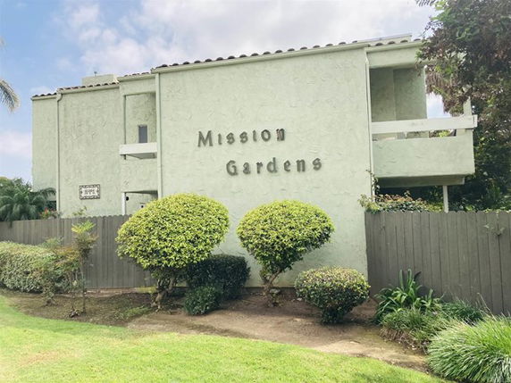 Front view of a multi-story building with a sign reading 'Mission Gardens' on the wall.
