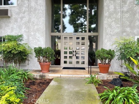 Front view of a building entrance with double glass doors and potted plants.