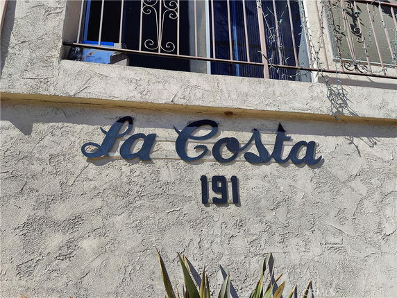 Front view of a building with the name 'La Costa' and number '191' displayed on the wall below a window with metal bars.