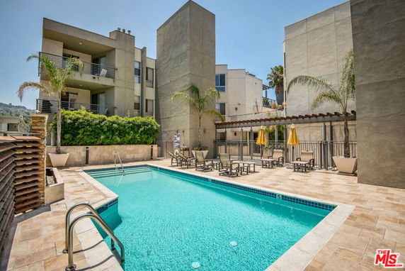Outdoor swimming pool area with lounge chairs and nearby buildings.