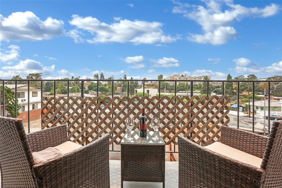 Outdoor seating area with wicker chairs and a table on a balcony, overlooking urban surroundings.