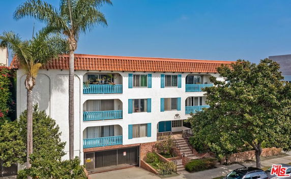 Front view of a multi-story apartment building with balconies and a tile roof.