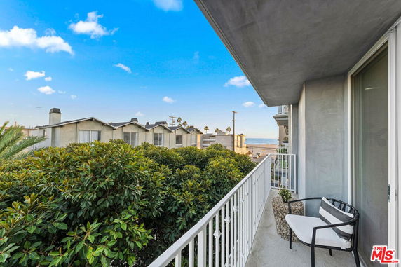 Balcony view overlooking nearby buildings and ocean in the distance.