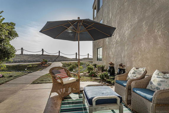 Outdoor seating area with wicker chairs under an umbrella, adjacent to a building.