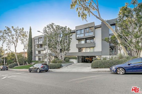 Front view of a multi-story residential building with trees and parked cars.