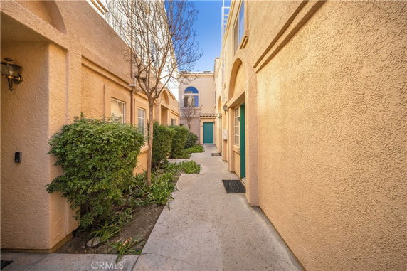 Facade of a stucco building with narrow walkway and small windows.