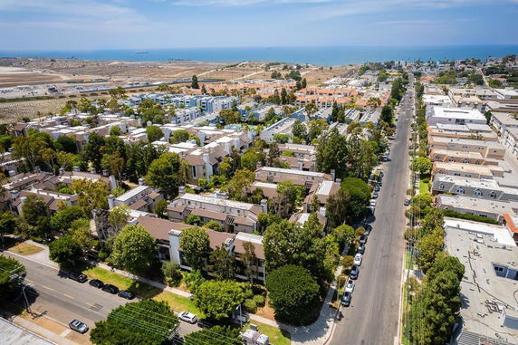 Aerial view of residential area with buildings and roads, overlooking the ocean in the distance.