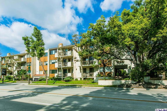 Front view of a multi-story apartment building with balconies and trees surrounding it.