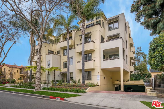 Front view of a multi-story apartment building with balconies and surrounding trees.