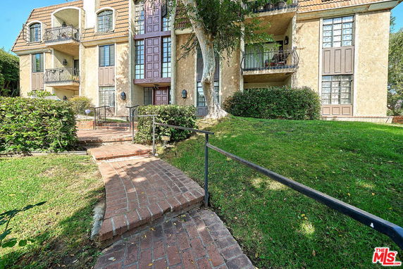 Front view of a multi-story residential building with balconies and a brick walkway.