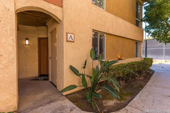 Entrance view of a residential building with a labeled door and nearby vegetation.