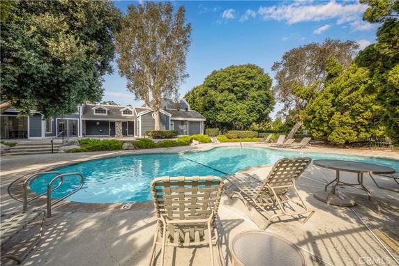Outdoor area with a large swimming pool, surrounded by patio furniture and lush trees, adjacent to a building.