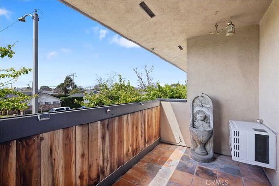 Balcony with wooden railing and tile flooring overlooking surrounding neighborhood.