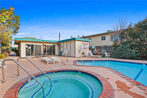 Outdoor swimming pool area with lounge chairs and a building in the background.