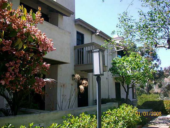 Front view of a two-story house with balconies and surrounding greenery.