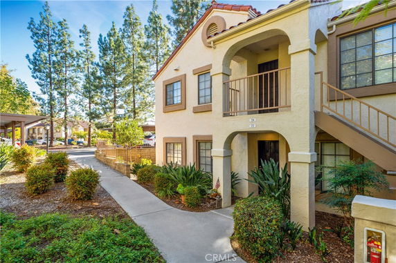 Front view of a two-story residential building with an external staircase and landscaped surroundings.