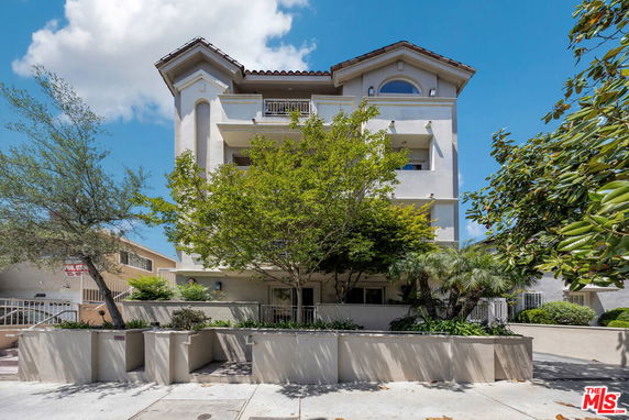 Front view of a multi-story building with balconies and a sloped roof.