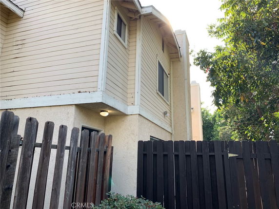 Side view of a two-story house with wooden siding and a fence.