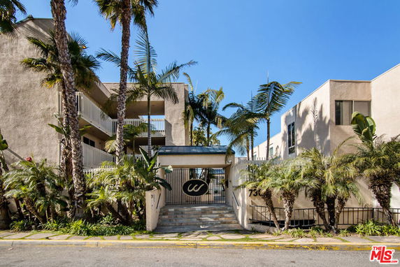 Front view of a multi-story building with a gated entrance and palm trees.