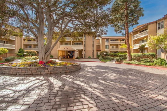 View of a multi-story residential building with a central courtyard featuring a large tree and flower beds.