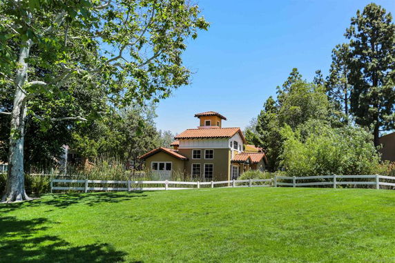 Front view of a multi-story house with a red-tiled roof and a fenced yard.