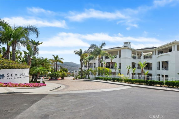 Front view of a multi-story white building with balconies and landscaped surroundings.